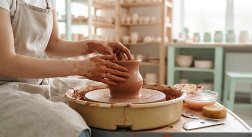 Hands shaping a wet clay terracotta vessel on an electric potter's wheel